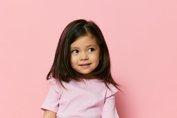 close horizontal portrait of a funny little girl pleasantly smiling standing on a pink background with empty space for inserting an advertising mockup