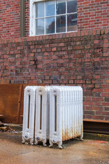 Three discarded radiators outside old brick residential building in New Orleans, LA, USA