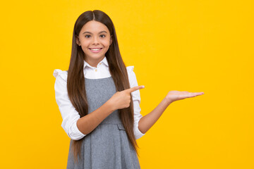 Positive teenager child points aside with cheerful expression, shows amazing at blank empty space. Advertisement and mockup. Happy girl face, positive and smiling emotions.