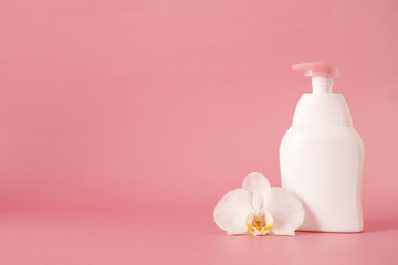 Obraz na płótnie Canvas white cosmetic plastic bottle with pump dispenser pump and with orchid flower on pink background. Liquid container for gel, lotion, cream, shampoo, bath foam.