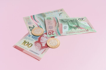 Nuevo billete de veinte pesos. Nuevo billete de cien pesos. Moneda de diez pesos. Moneda de dos pesos sobre fondo rosa. 