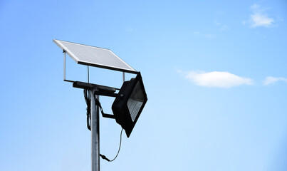 Mini photovoltaic or solar cell panel and floodlight led installed on metal pole against blue sky...