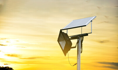 Mini photovoltaic or solar cell panel and floodlight led installed on metal pole against sunset sky...