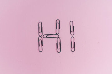 Clips negros, para sujetar papel, sobre fondo rosa. Palabra Hi.
