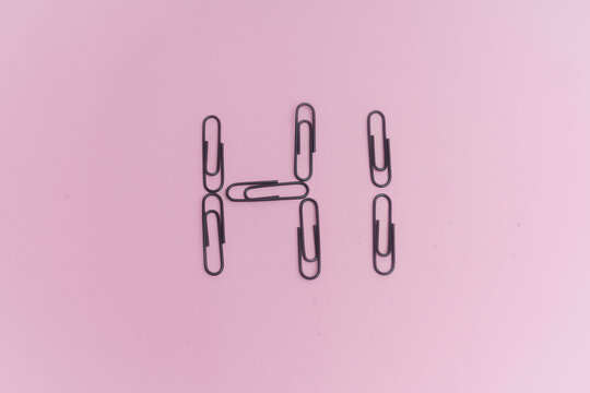Clips negros, para sujetar papel, sobre fondo rosa. Palabra Hi.