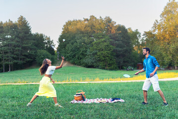 Young smiling couple playing badminton during picnic on the meadow