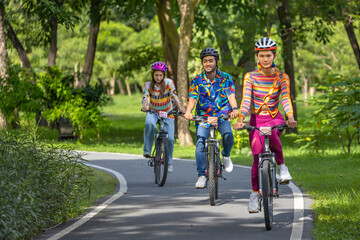 Team of Asian cycling friends riding in the public park inside bike lane with bicycle on the bridge with the green forest background