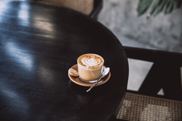 Glass of cappuccino with latte art on saucer and with spoon on the black table