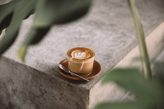 Glass of cappuccino with latte art on saucer and with spoon on the concreet background