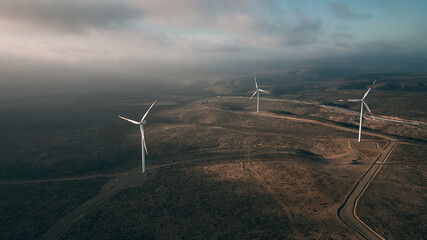 Wind turbines on beautiful sunny summer autumn mountain landsape. Curvy road through mountain Eolic...