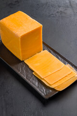 cheddar cheese sliced on black plate on dark table, vertical