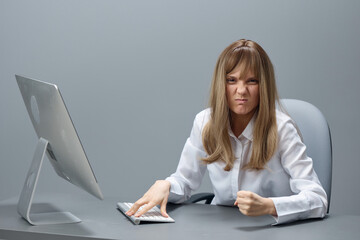 Irritated pretty blonde businesswoman worker freelancer show fist using desktop computer sitting at workplace in gray modern office. Remote Job, Technology And Career Profession Concept. Copy space