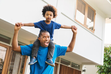 Cheerful Black African American Father piggyback or carrying his little son on his shoulder and...