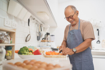 Happy smiling Asian Senior adult man chopping carrots on wooden board, Japanese or Chinese Mature Male cooking in kitchen, Preparing food.