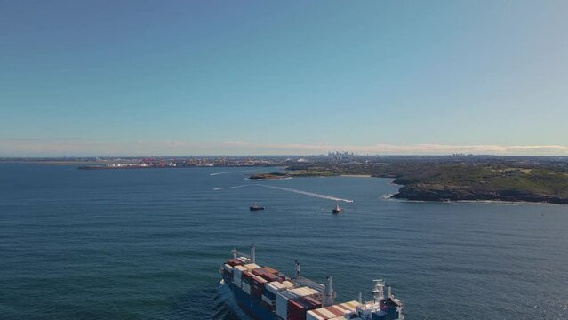 Aerial drone view of a large cargo container ship entering Botany Bay at the coastline of Kurnell and headland of Kamay Botany Bay National Park, Sydney, NSW heading to Port Botany on a sunny day  