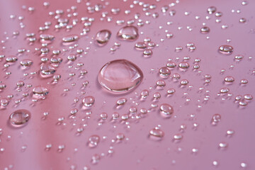 A large drop and splashes of micellar water on a pink background.