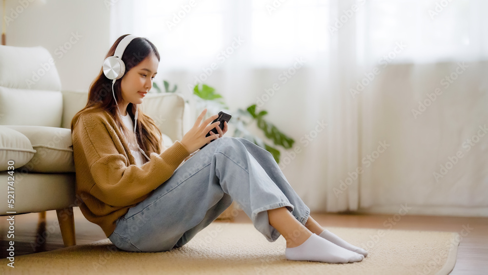 Wall mural happy young asian woman relaxing at home. female smile sitting on sofa and holding mobile smartphone