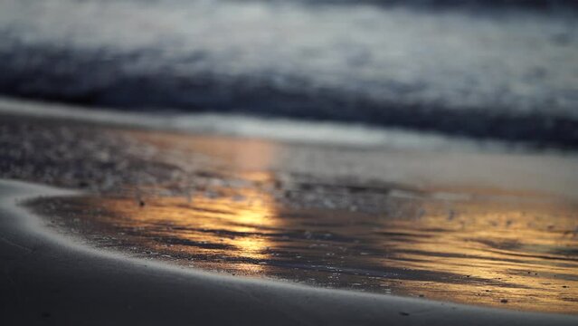 sunrise reflecting on the beach with golden light as waves roll in and water moves on the sand, calming waves	
