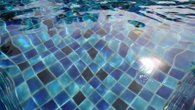Outdoor swimming pool with the sun reflection on the surface of the water and blue porcelain tiles