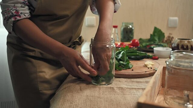 Close-up. Filling sterilized glass jar with chopped fresh dill leaves, garlic when pickling seasonal vegetables in the kitchen. Canning food and making preserves for the winter. Pickling. Marinating