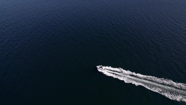 Aerial footage of a speed boat racing across the ocean, waves, boat wake, sunny day summer, happy life, luxury life. 5.4K to 4K 24FPS.