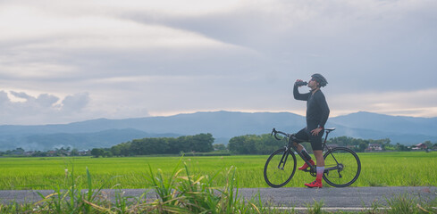 A cyclist or sport bicycle drinking water during take a break against beautiful view in the middle of the rice field.