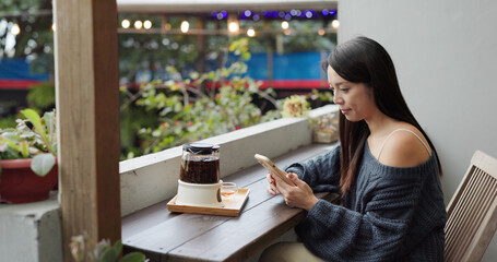 Woman look at mobile phone and drink of hot tea at outdoor coffee shop