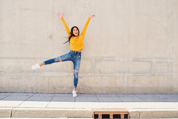 Happy young woman jumping against concrete wall in the city