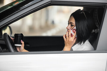 young beautiful brunette woman driver sitting in her car with a glass of coffee and talking on the phone