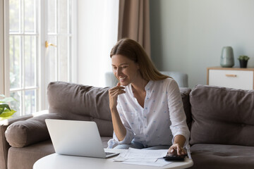 Young woman sits at table with laptop, counts profit and income, makes expenses and receipts analysis, paying bills looks satisfied, enough funds for utility bills payments. Finances, wealth concept