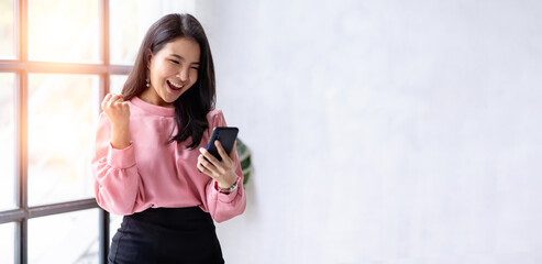 Excited happy Asian woman looking at the phone screen, celebrating an online win, overjoyed young...