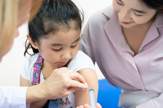 Young Asian girl get medical vaccination from the doctor with her mother sit and hold to support. Medical service for young people, kids. Immunity dose injection to prevent illness in children.