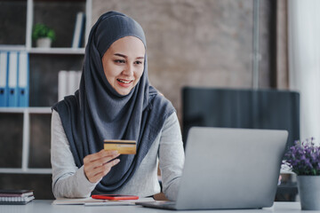 Portrait of a Muslim businesswoman shopping on her credit card phone. smiling arab woman taking notes and work on laptop