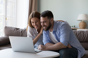 Couple staring at laptop screen smile enjoy good news, reading received notification feel satisfied spend time using modern device. Wireless technology, marketplace on-line, e-shopping at home concept