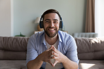Smiling man wear headphones looks at camera makes videoconference participates in on-line stream,...