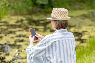 woman wearing in hat sitting in the park on the green grass with a smartphone