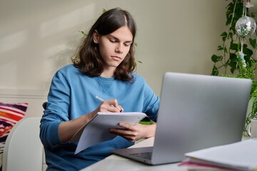 Teenage male student studying at home using a laptop