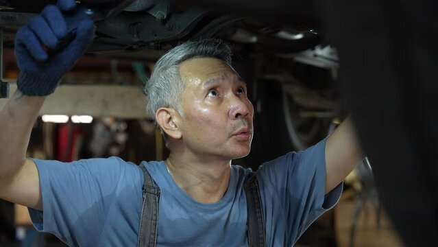mechanic technician work to fixing repair car undercarriage at auto garage, vehicle inspection station for automobile maintenance service workshop, person using automotive industry tool for work