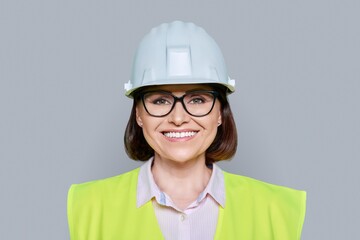 Female industrial worker in protective hard hat and vest on gray background - Powered by Adobe