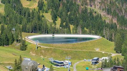Artificial water catchment reservoir for snow skiing slopes at Dolomites in Italy. Summer view