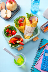School lunch box for kids with sandwich, vegetables, water and stationery on table. Healthy eating...