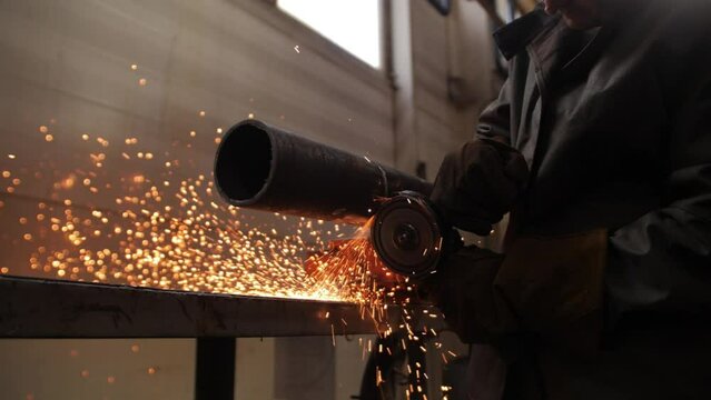 Male hand cuts off pieces of water pipe with angle grinder. Cutting of a steel with splashes of sparks at construction site. Sparks during cutting of metal angle grinde