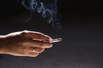 Close-up of a woman's hand holding a cigarette. Tobacco butt with clouds of smoke on a dark...
