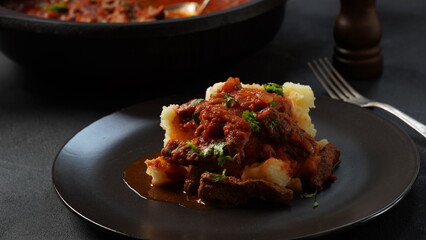 Beef stew with tomato sauce, spices and herbs on mashed potatoes.