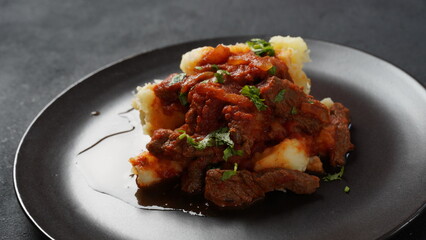 Beef stew with tomato sauce, spices and herbs on mashed potatoes.