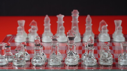 Transparent chess figures, on starting position, on reflective chess board, red tone. Strategic Chess board game