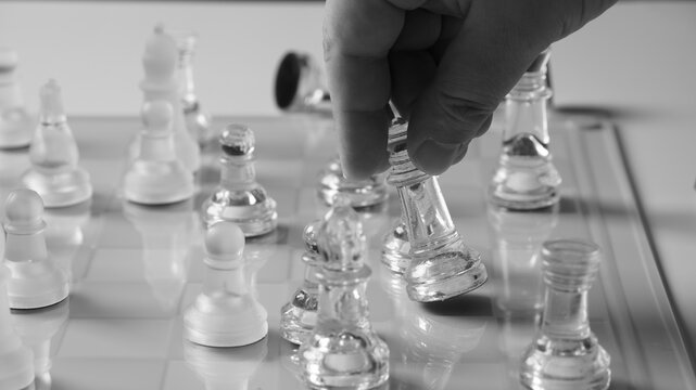 A chessboard with a hand starting to move a chess piece. Clear glass chess figures on a chessboard