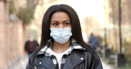 Young woman wearing protective face mask in a city. Masked african-american girl on a city street. Epidemic, pandemic, corona virus protection, healthy lifestyle, people concept.