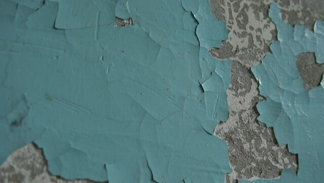 Crack on a blue and gray painted concrete wall. Textured background pattern of rough and damaged surface detail shot. Slow motion tilt.