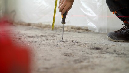  worker's hand with a screwdriver is screwing a screw into a concrete floor. Installation of beacons on the floor. A worker drives a screw into the floor. Floor renovation concept.